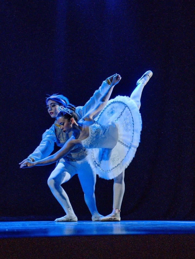 Un pas de deux de alumnas avanzadas en una función, bajo luz azul